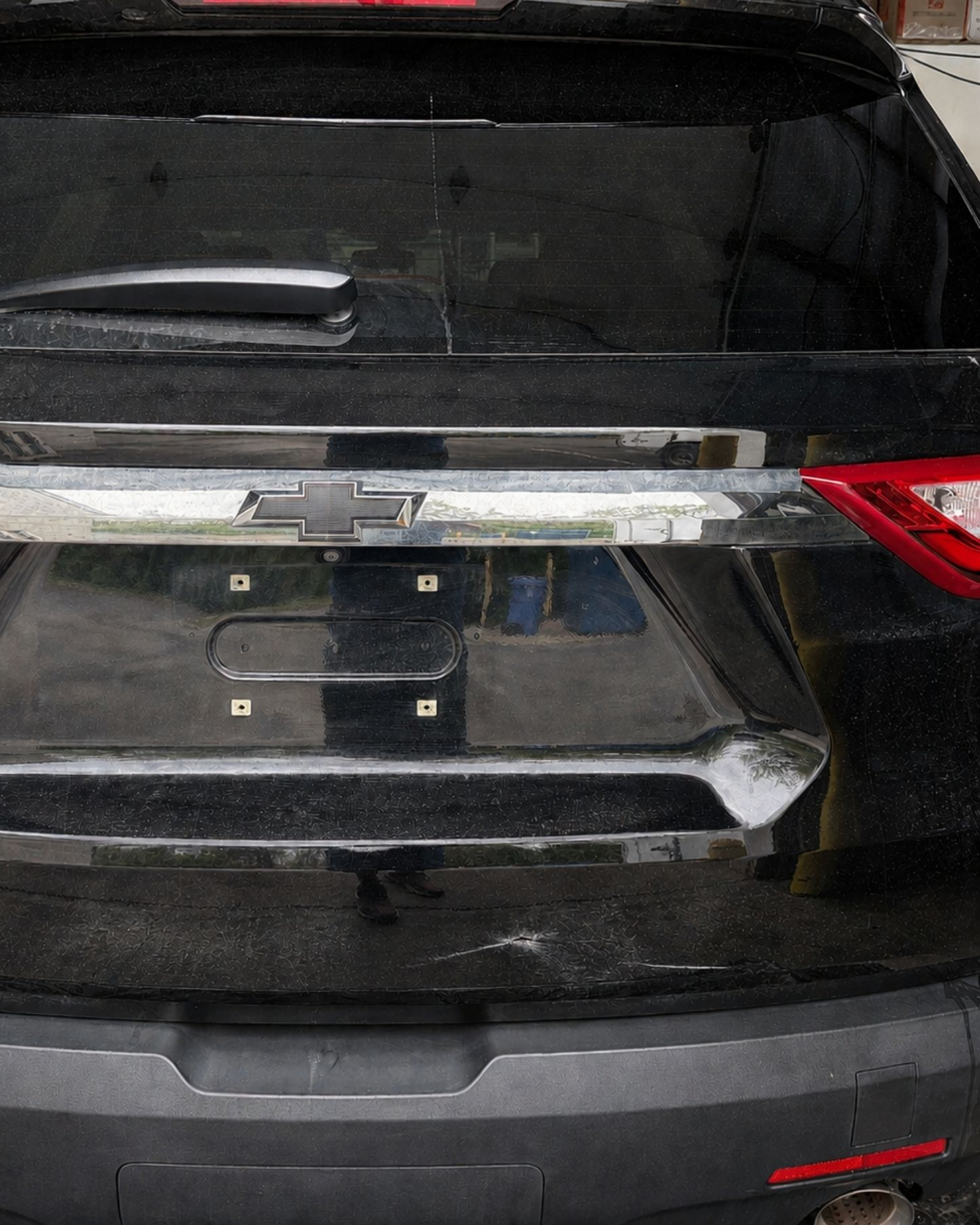 Black SUV rear with damaged/hanging chrome trim above an empty license plate holder