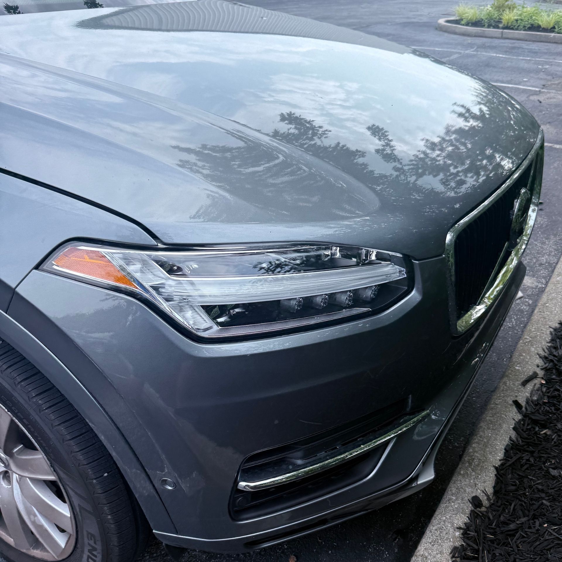 Close-up of a dark gray SUV’s front headlight and grille parked outdoors.