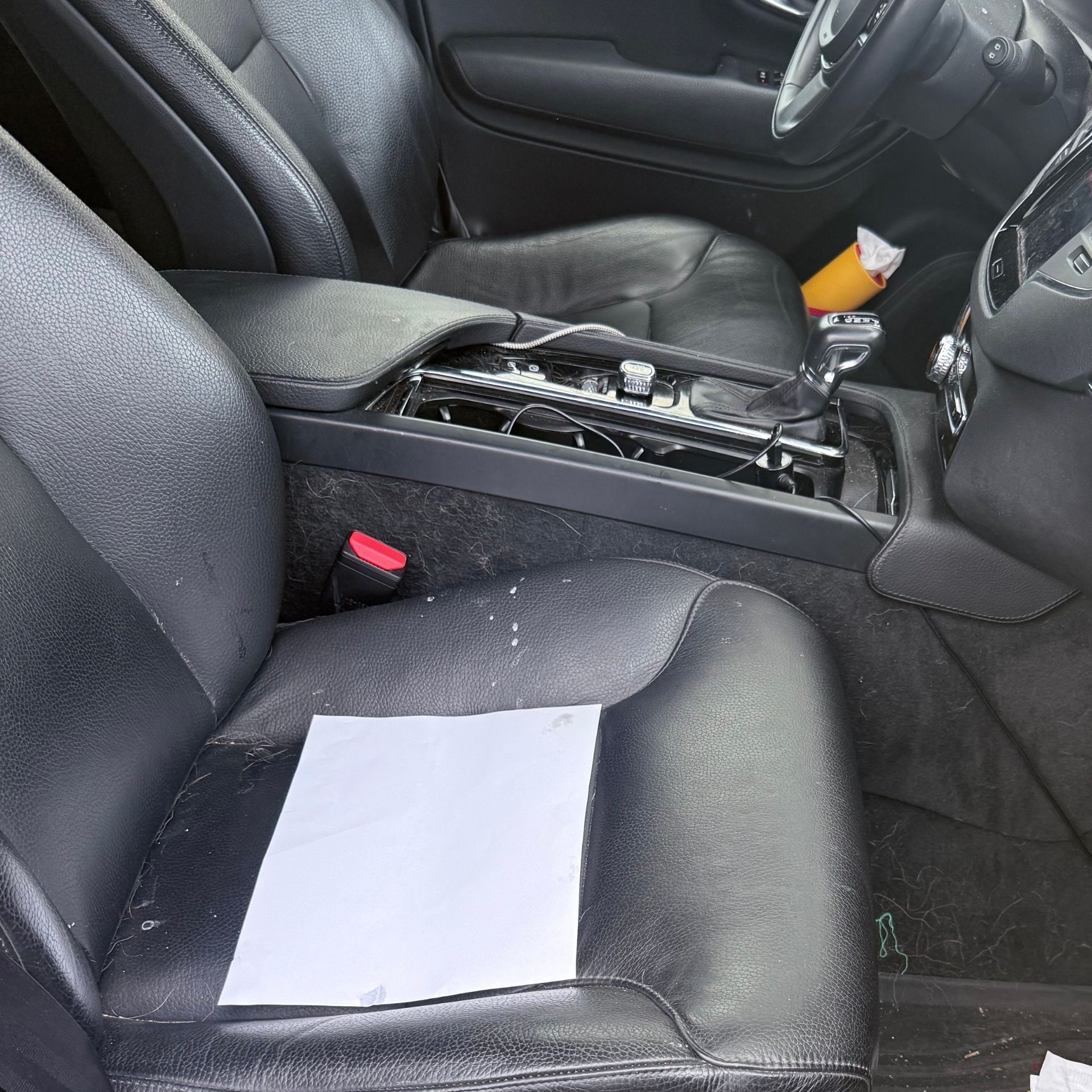 Car interior with a paper on the front passenger seat and the center console open, showing exposed wiring.