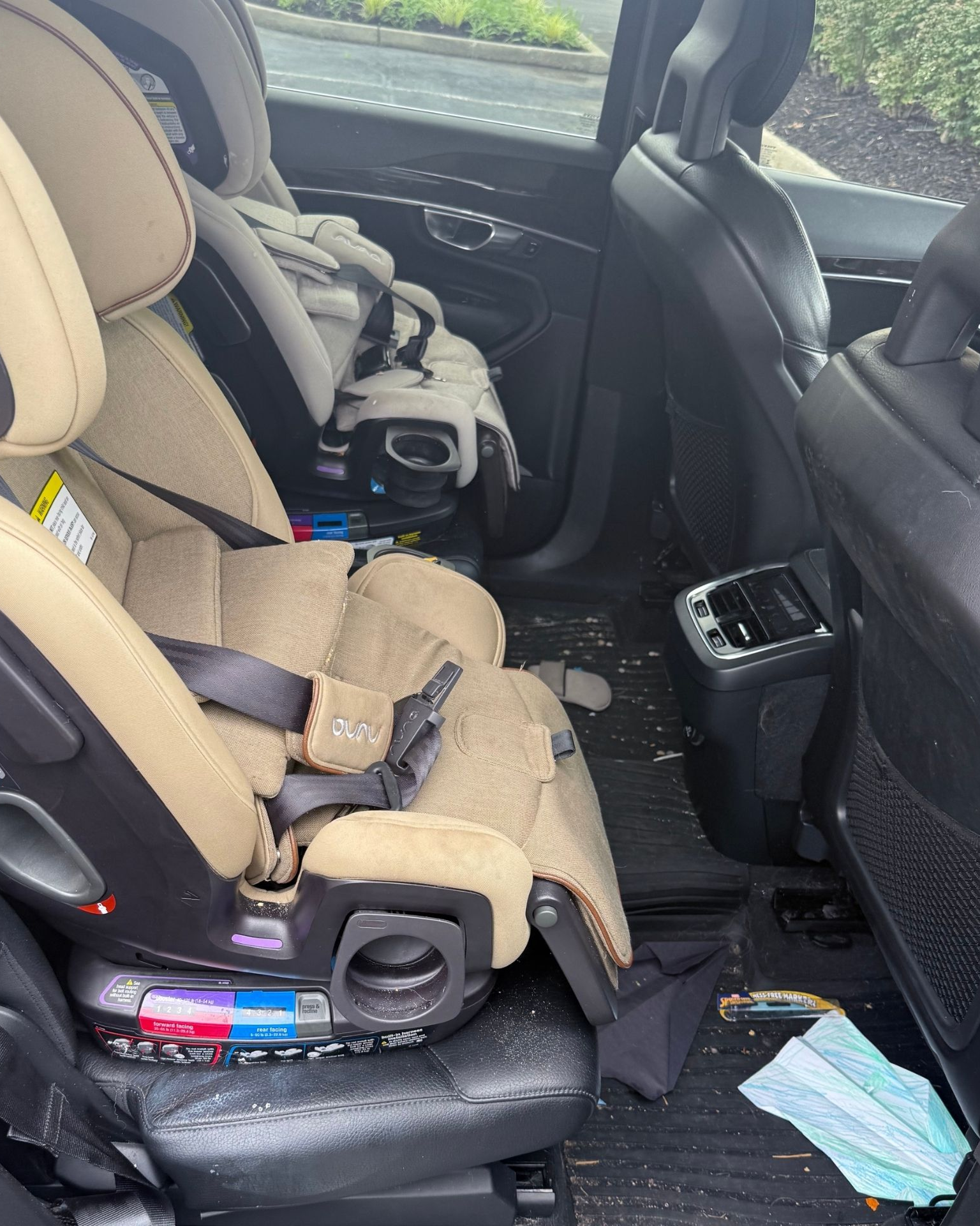 Two child car seats in the back of a vehicle, with a face mask on the floor.