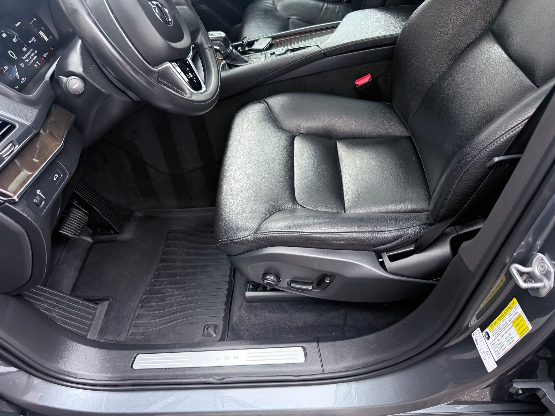 Car interior with black leather driver’s seat, steering wheel, and door sill visible