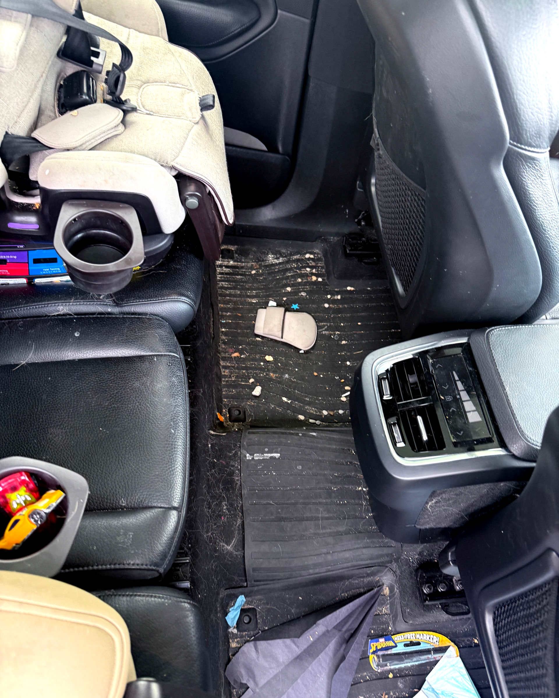 Car interior with spilled white debris on the floor between the seats and a dropped item near the rear vent.