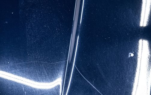 Close-up of a dark blue car surface with bright white reflections and a vertical panel seam
