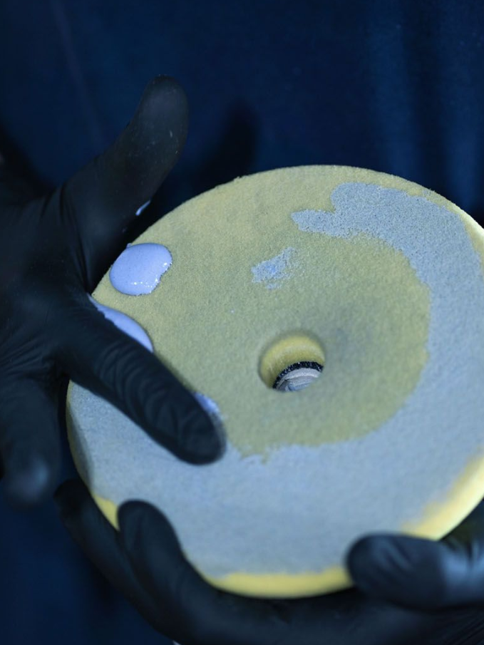 Gloved hands holding a yellow sanding disc with worn gray patches and a center hole