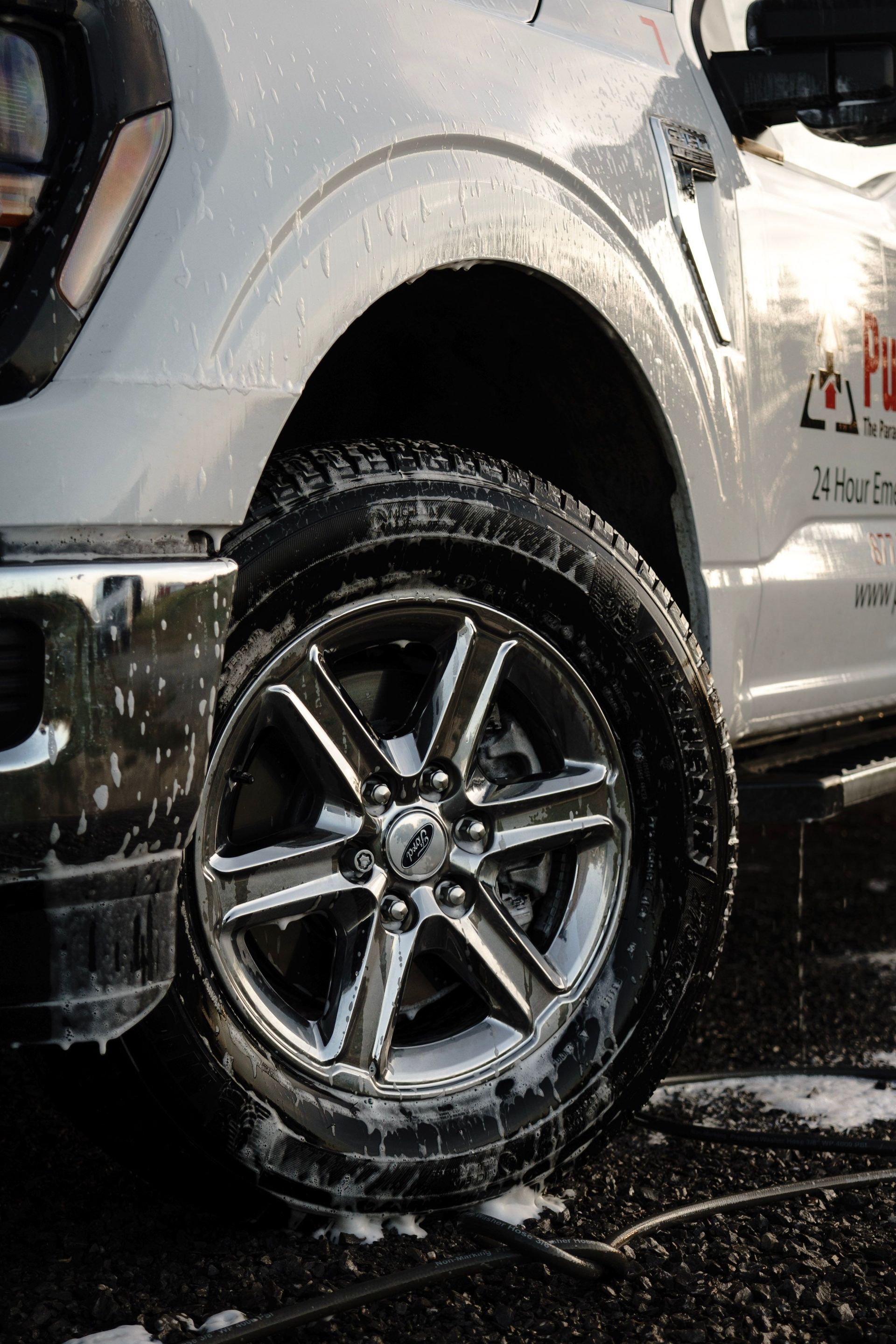 Close-up of a wet black SUV wheel and tire being washed with soap in a car wash.