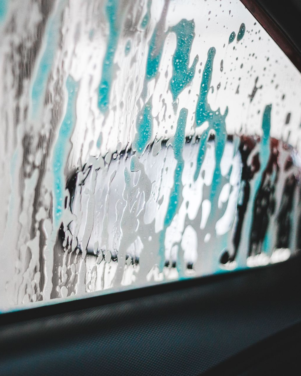 Rain-speckled car window with blurred turquoise and black graffiti outside