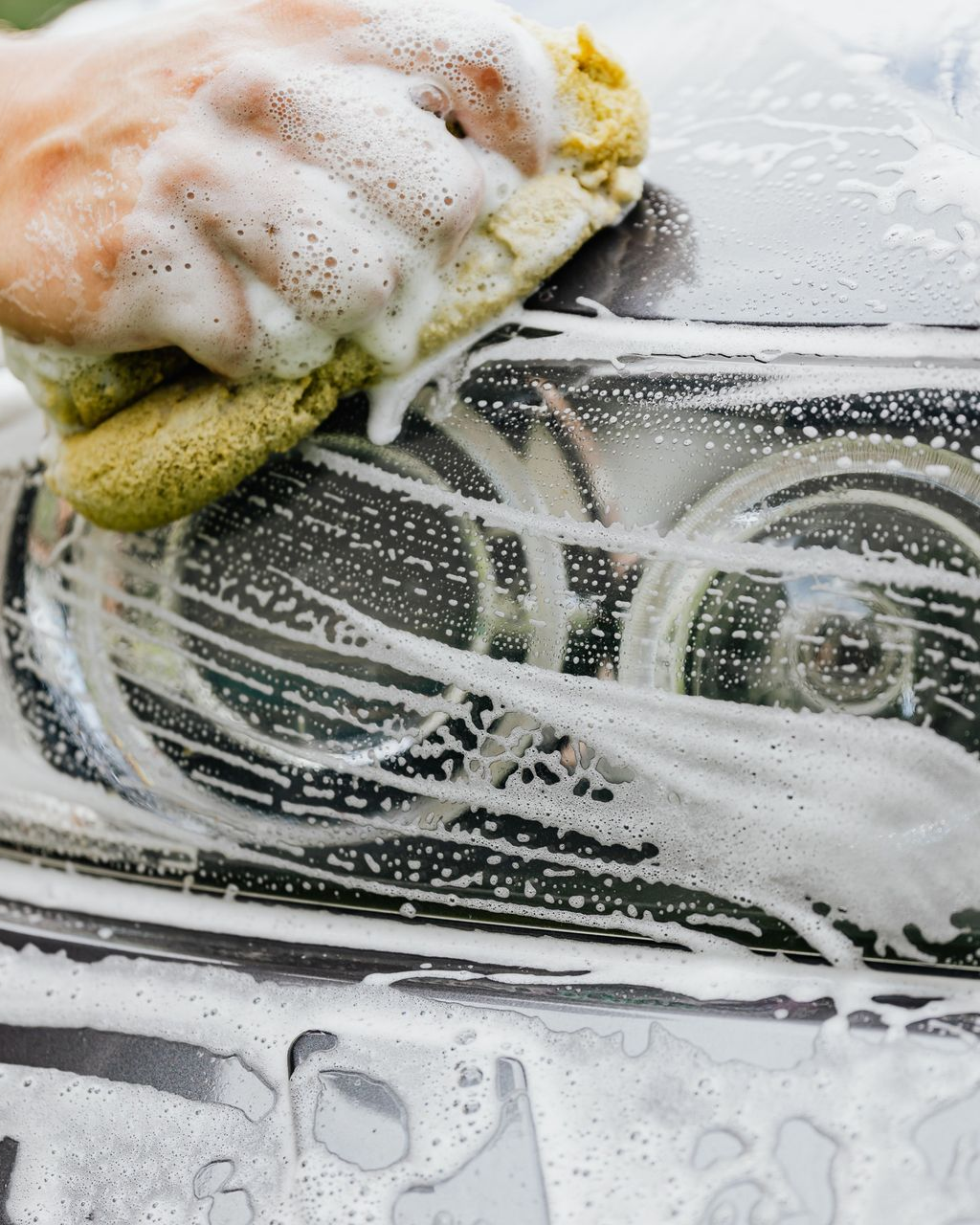 Person scrubbing a car window with soap and sponge, leaving white foam streaks