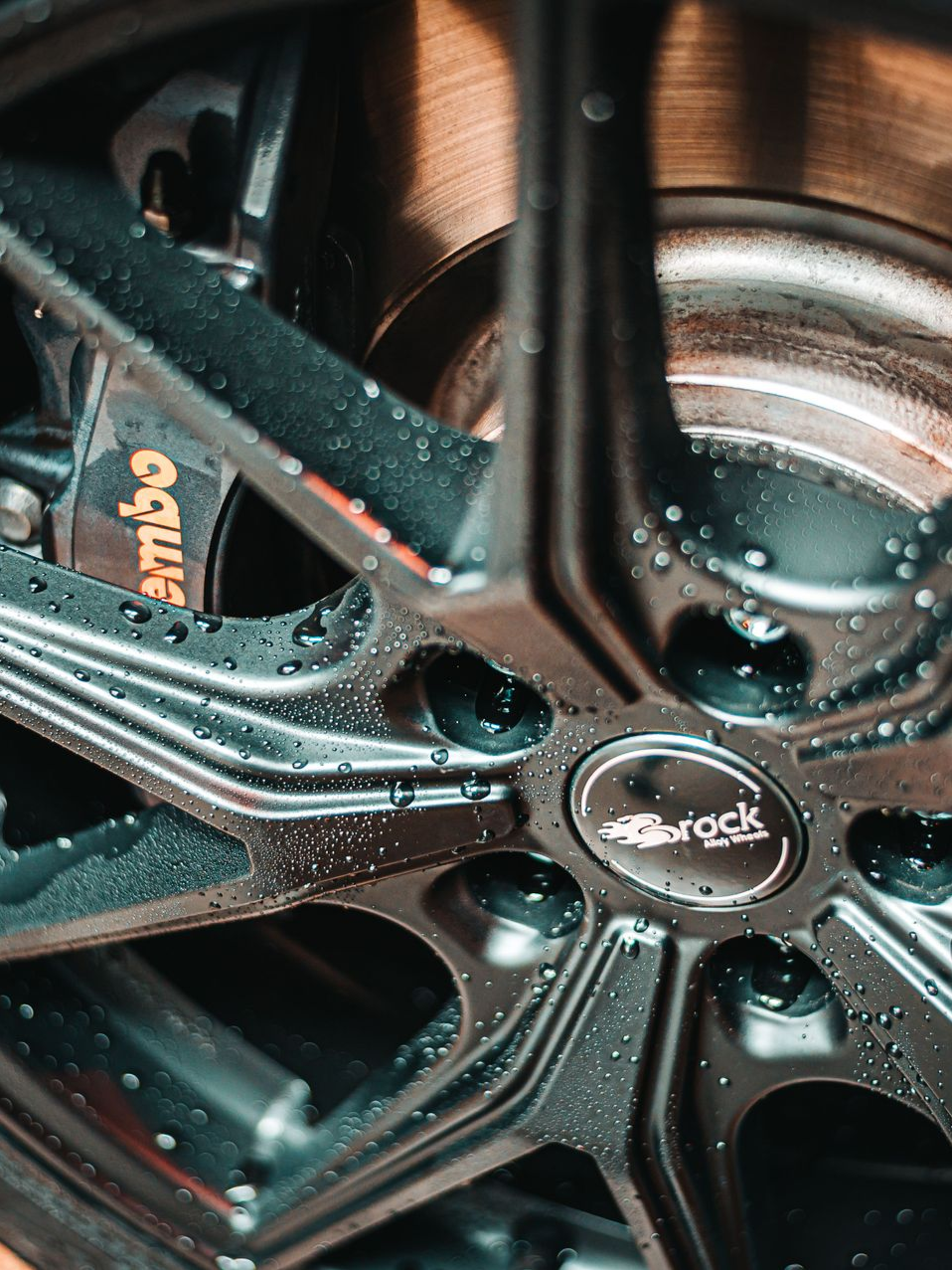 Close-up of a black alloy car wheel with a Brembo brake caliper and wet reflections