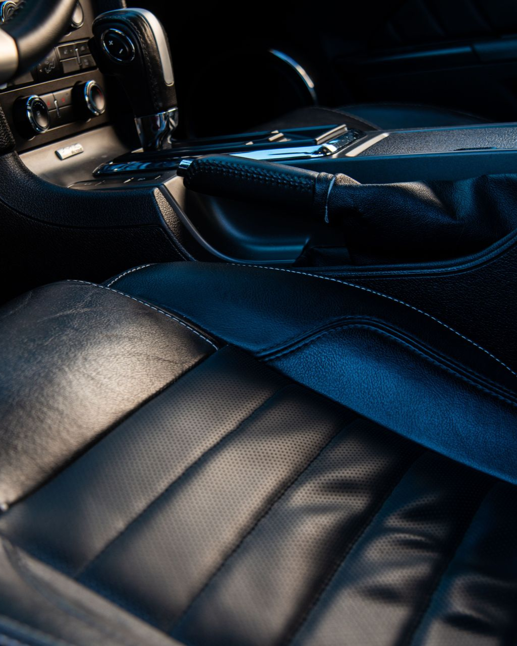 Close-up of a black car interior with seats, center console, and gear shifter in blue light