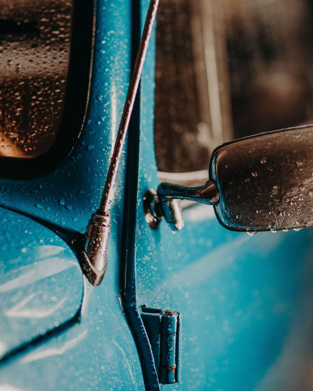 Close-up of a blue vehicle door and side mirror with raindrops on the surface