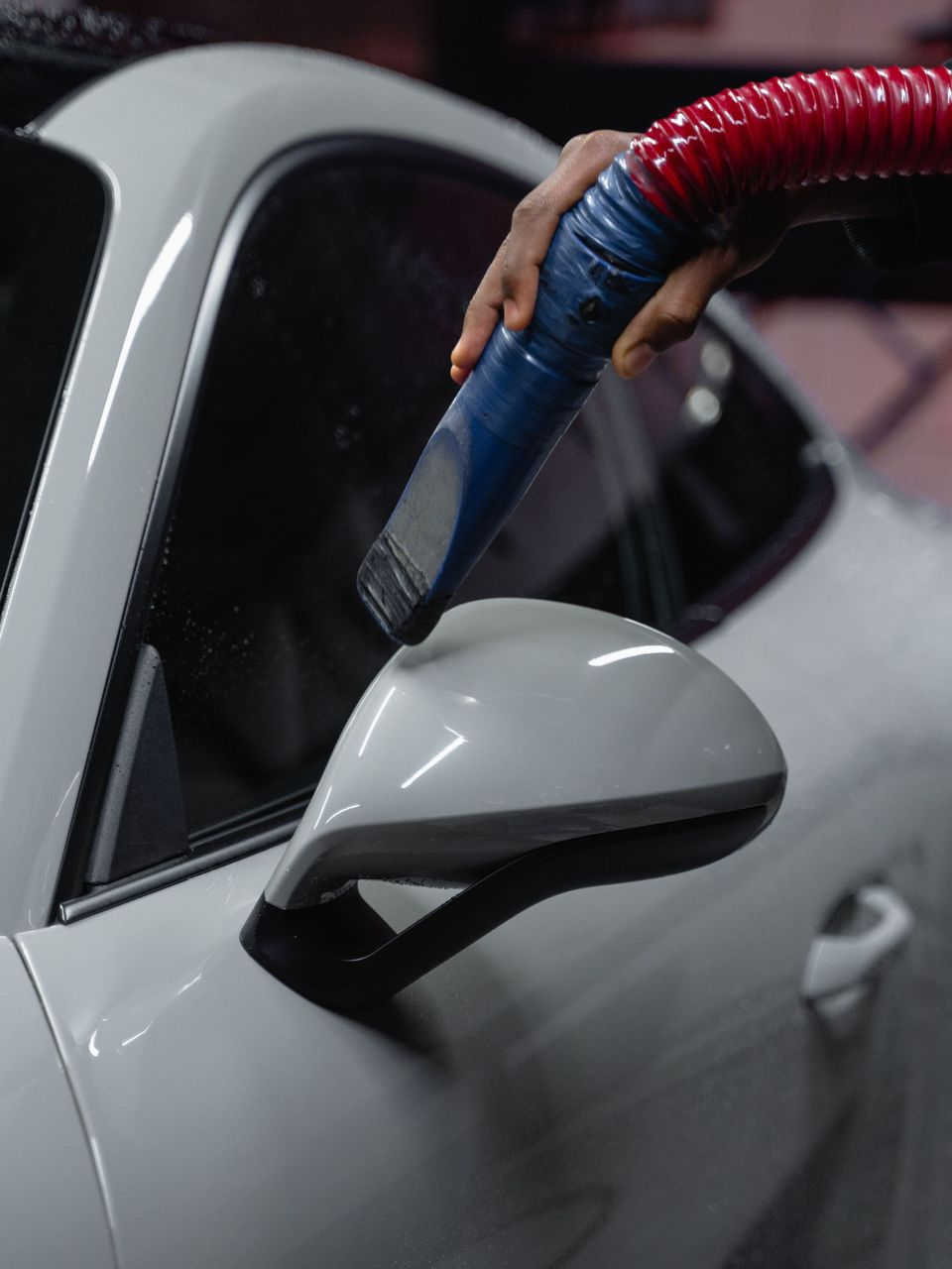 Vacuum hose cleaning the side mirror and window of a white car