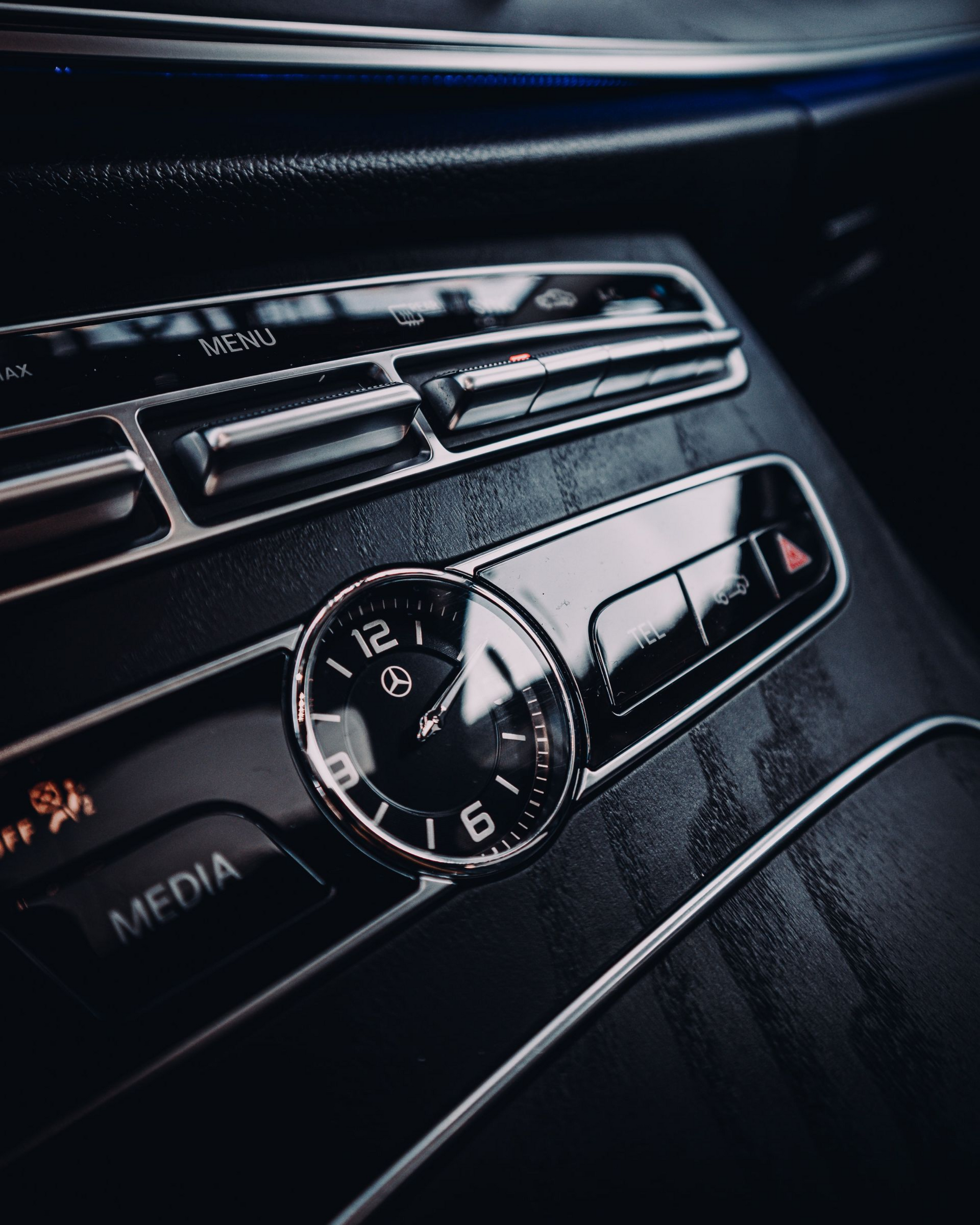 Car dashboard center console with chrome clock, vents, and media controls in dark interior