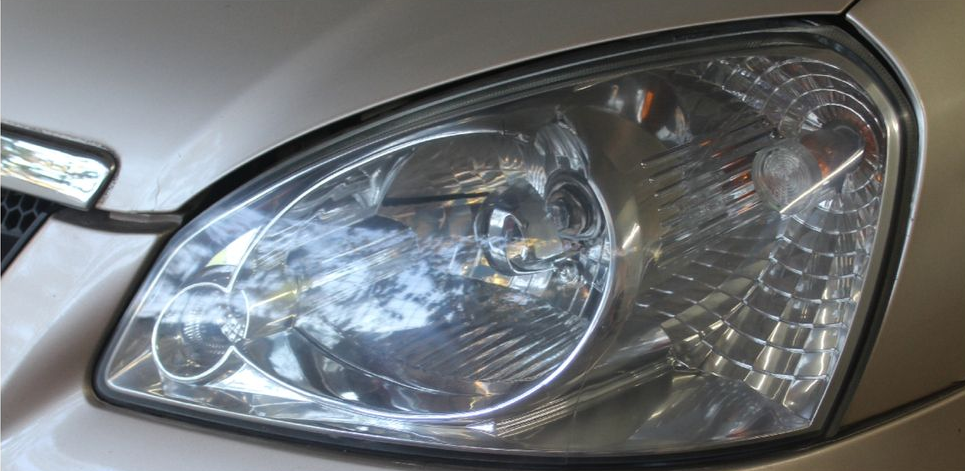 Close-up of a silver car’s front headlight and chrome grille