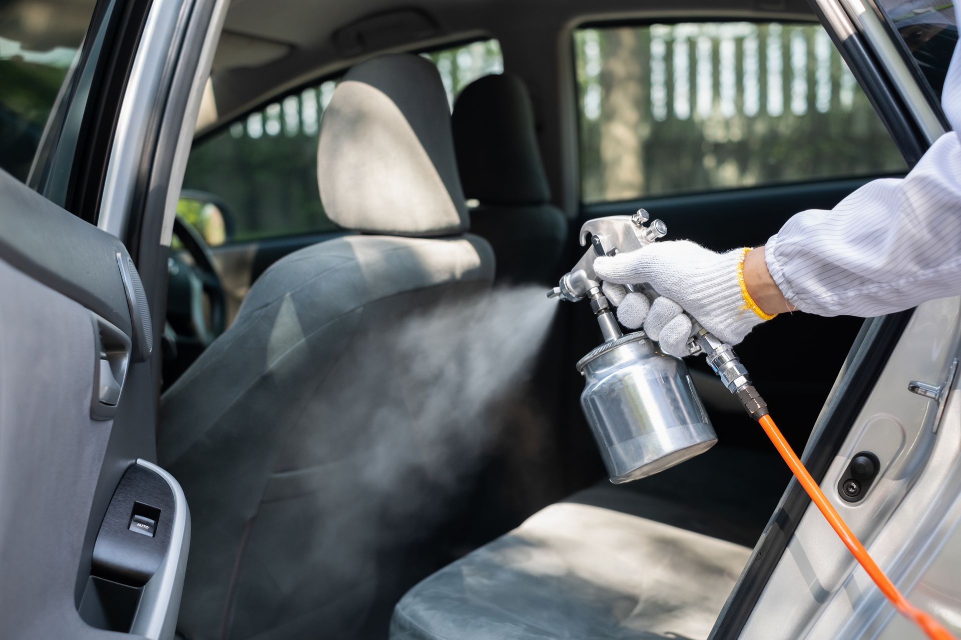 Person using a spray gun to clean a car’s front seat interior through the open door