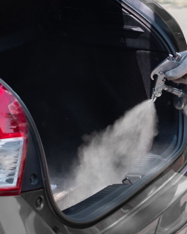 Black car trunk being cleaned with a pressure washer, spray mist inside the open cargo area