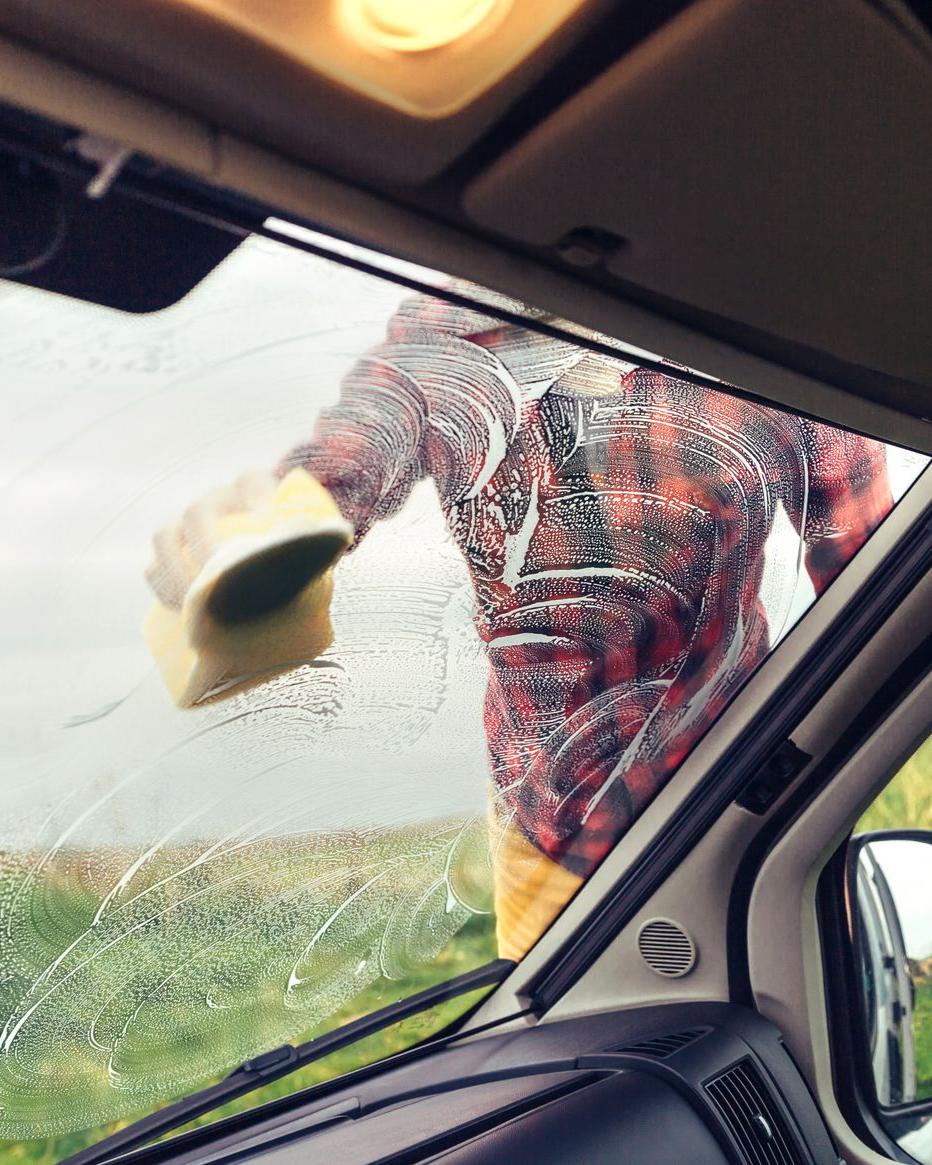 Person in red plaid shirt washing a car window with a sponge in the rain