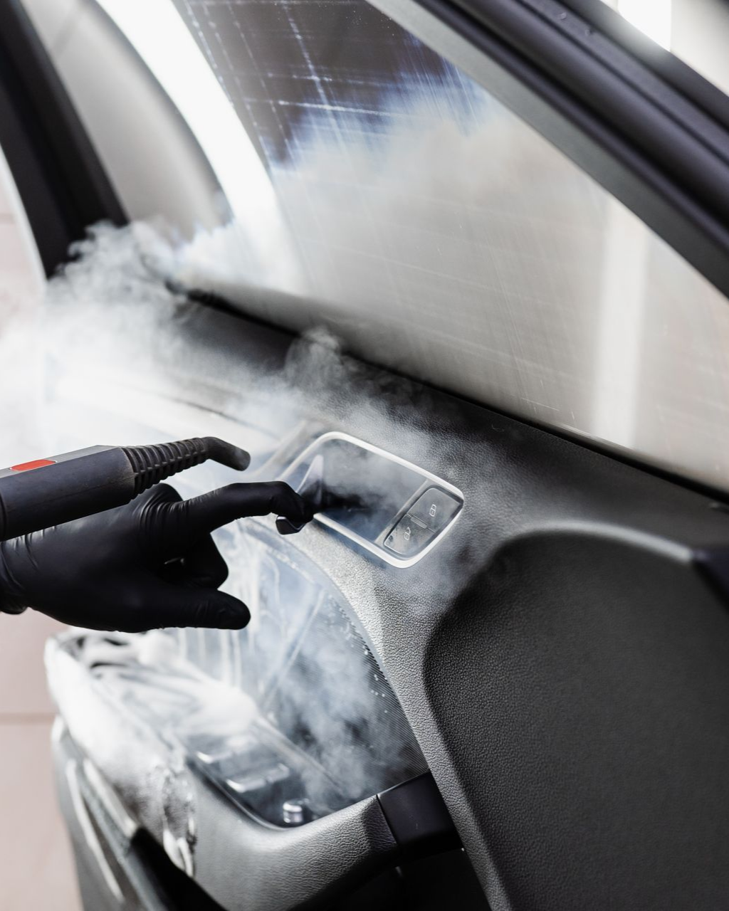 Person steam-cleaning a car door handle with a black cleaning tool, covered in white foam.