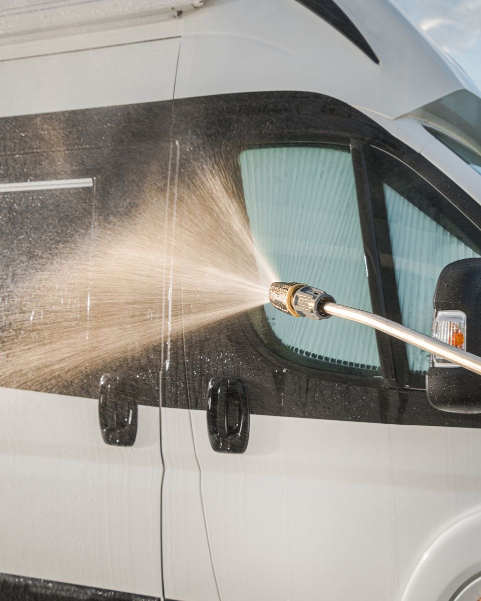 Pressure washing a white van's side window and body with a spray nozzle