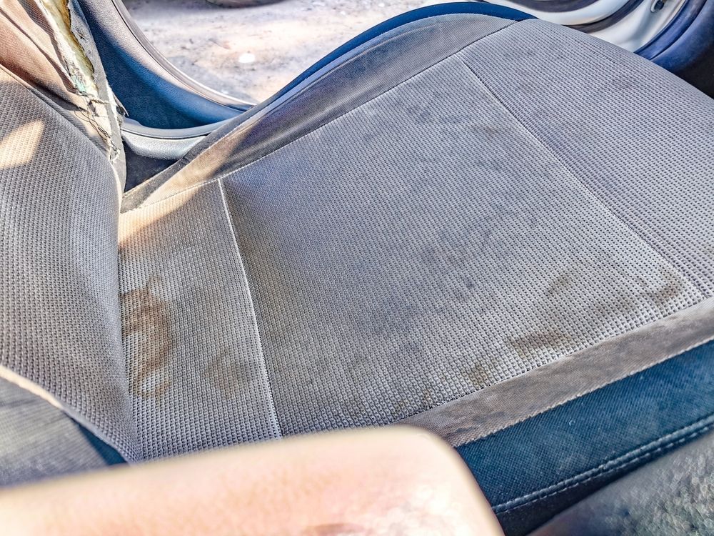 Close-up of a gray mesh car seat with visible dirt and stains on the fabric