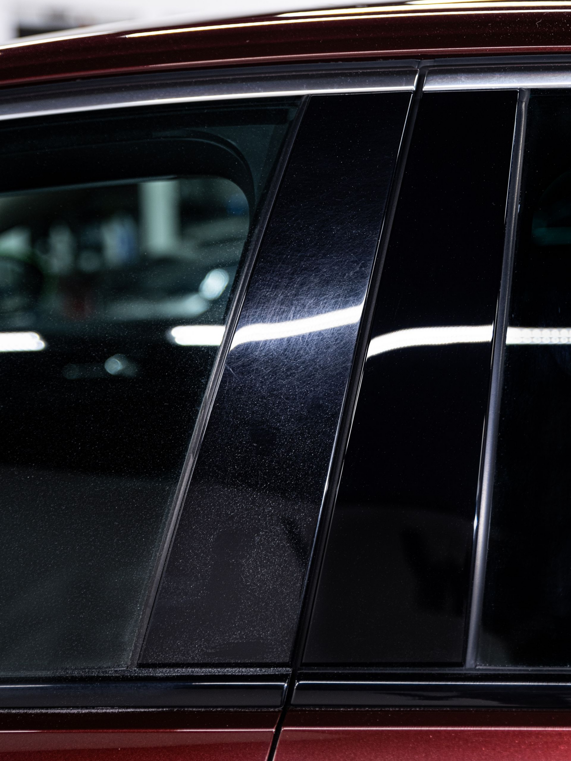 Close-up of a black car’s side window and pillar with a bright reflection on the glossy paint