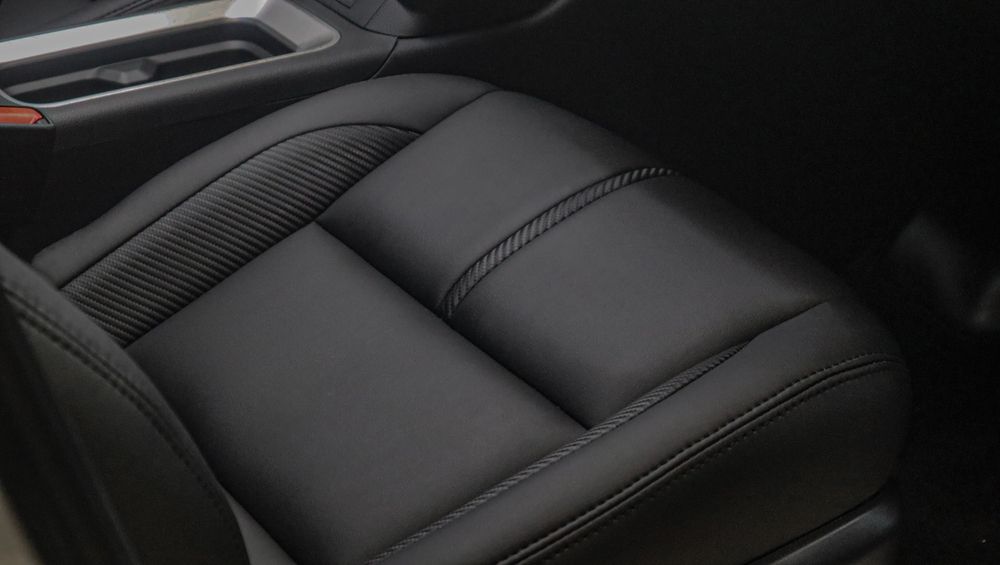 Black leather car seat with stitched panels and a center armrest console