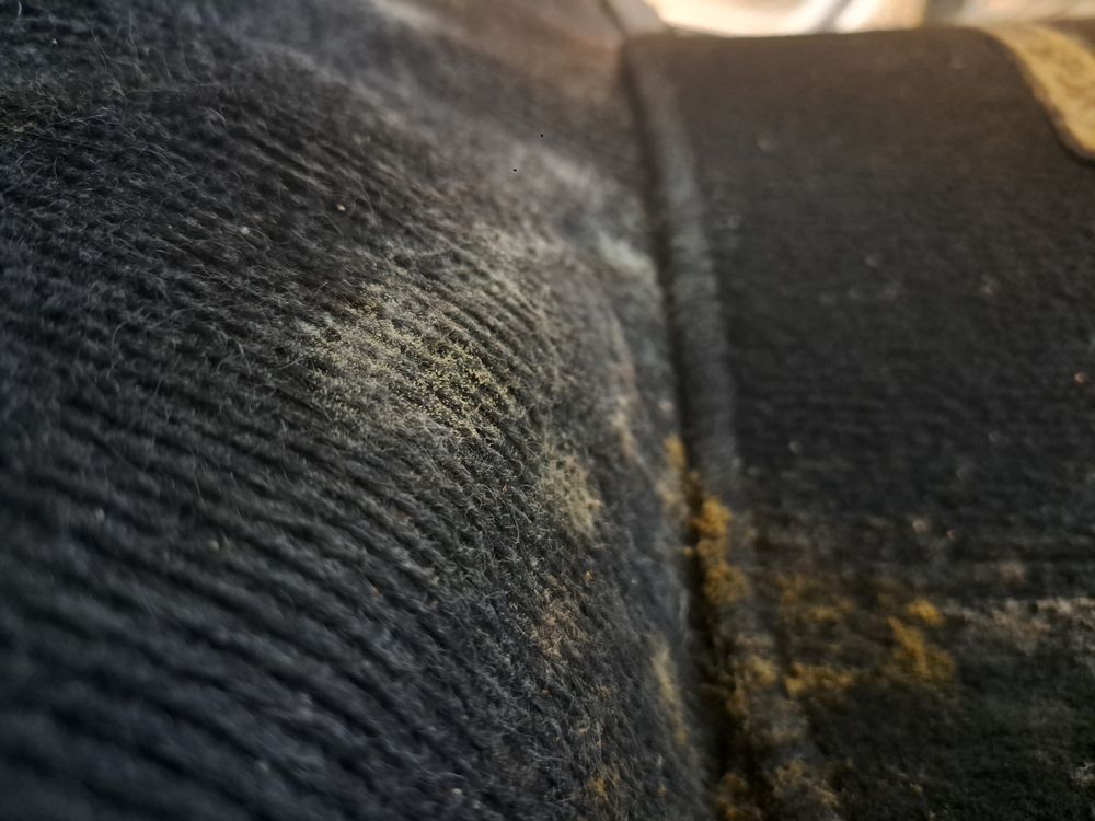Close-up of dark denim fabric with a seam and small tan stain