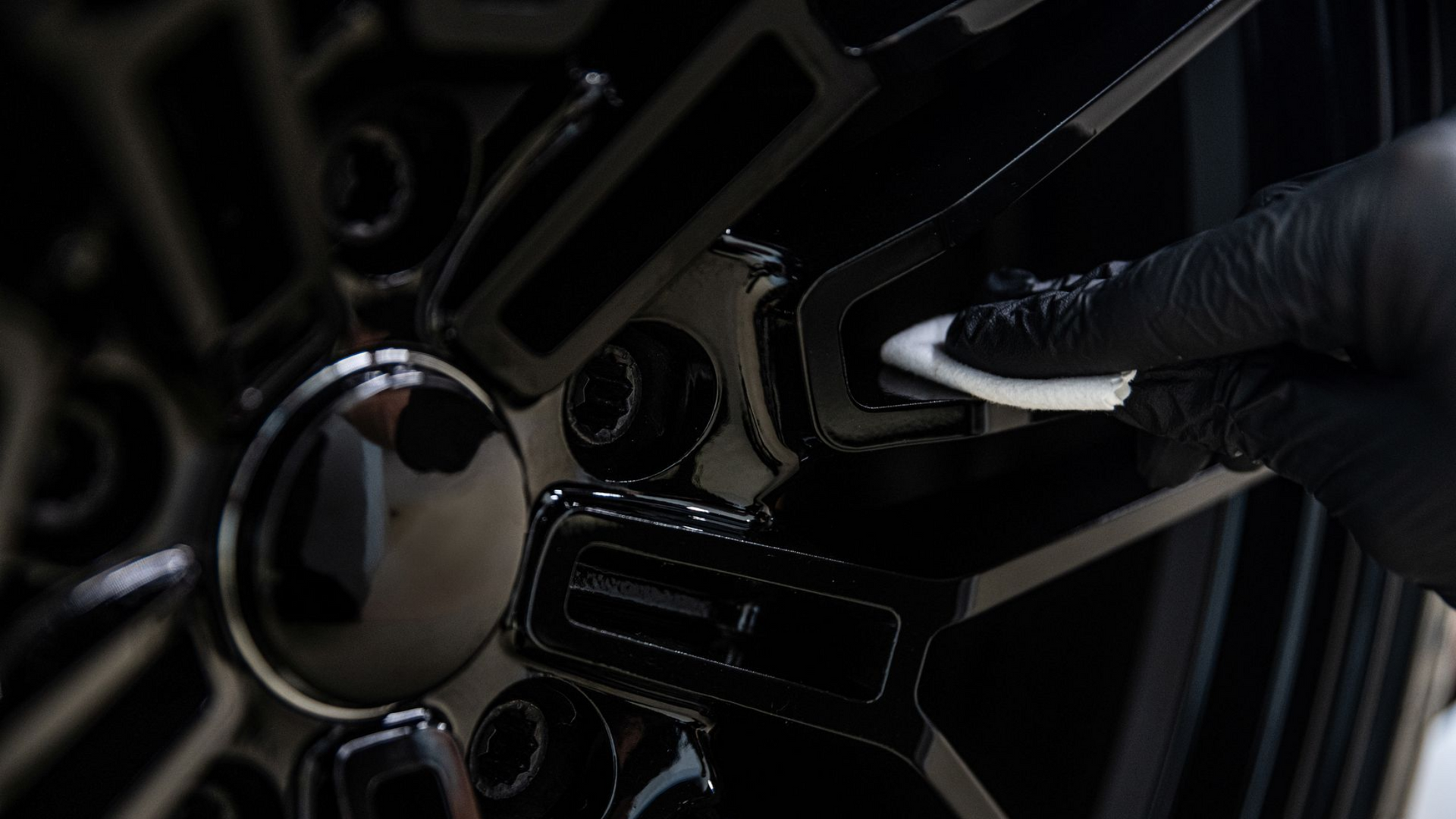 Gloved hand polishing a black car wheel rim with a cloth