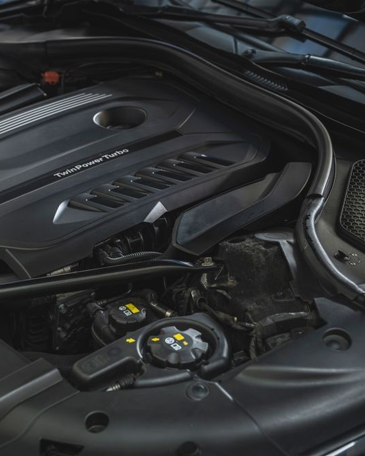 Car engine bay with black plastic cover and visible coolant reservoir cap in the foreground