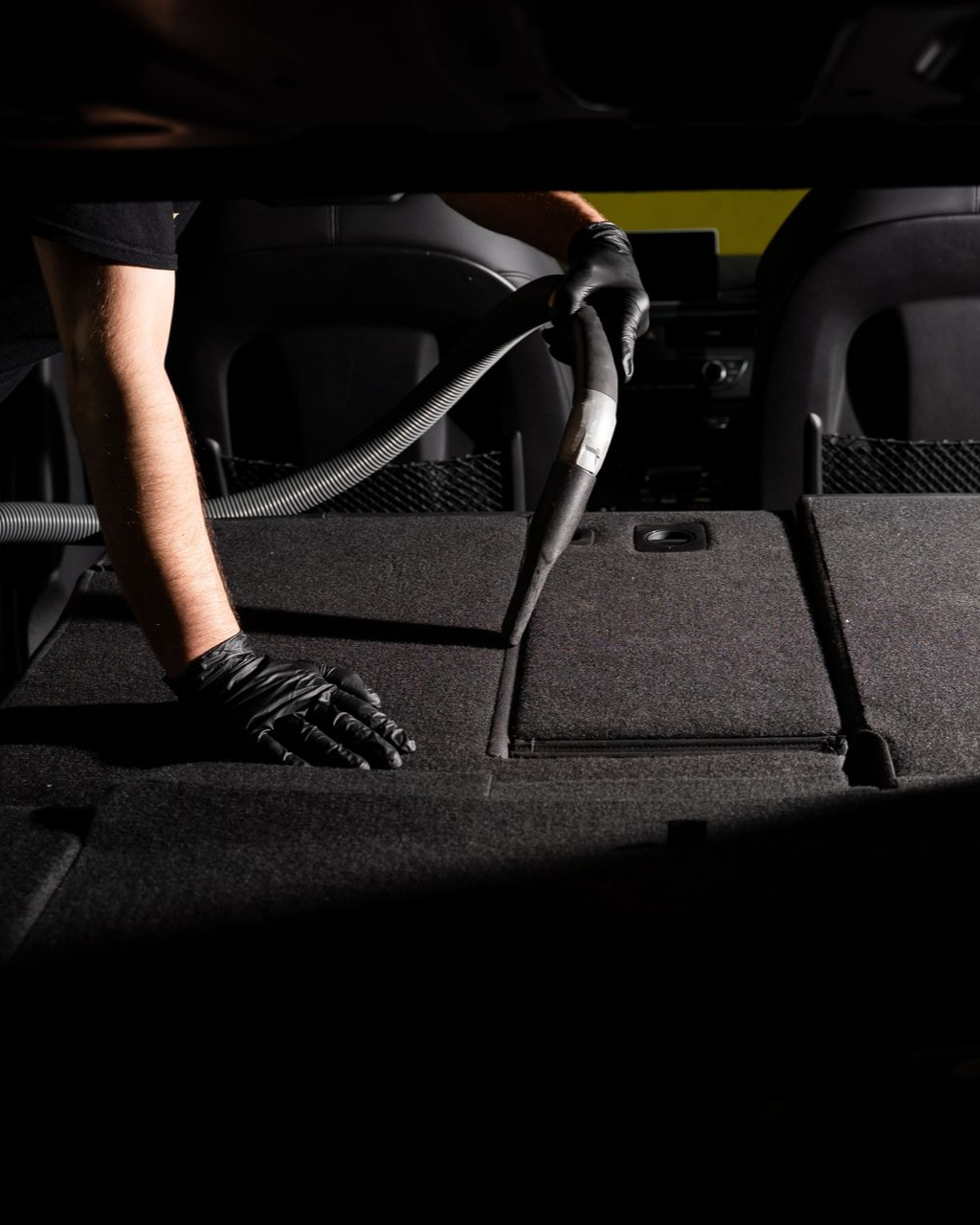 Person vacuuming the carpeted back seat of a car with a handheld nozzle