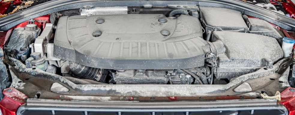 Car engine bay covered in white foam and snow, with the hood open on a wet street.