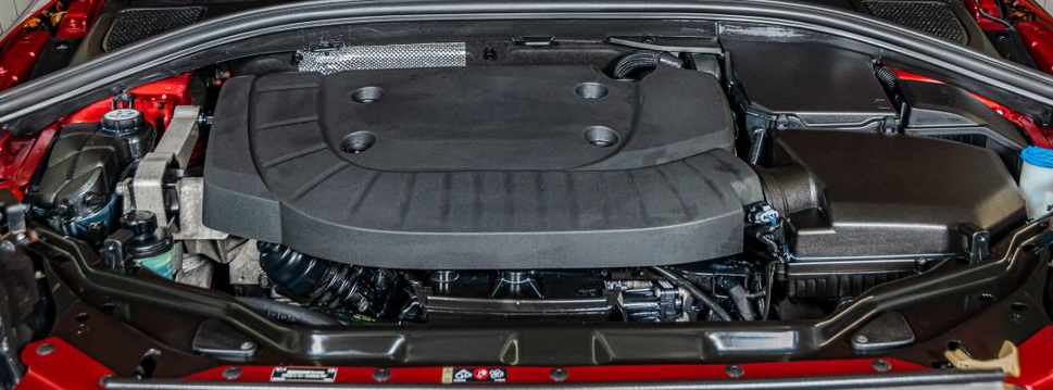 Car engine bay with a large black engine cover, red body panels, and visible hoses and components