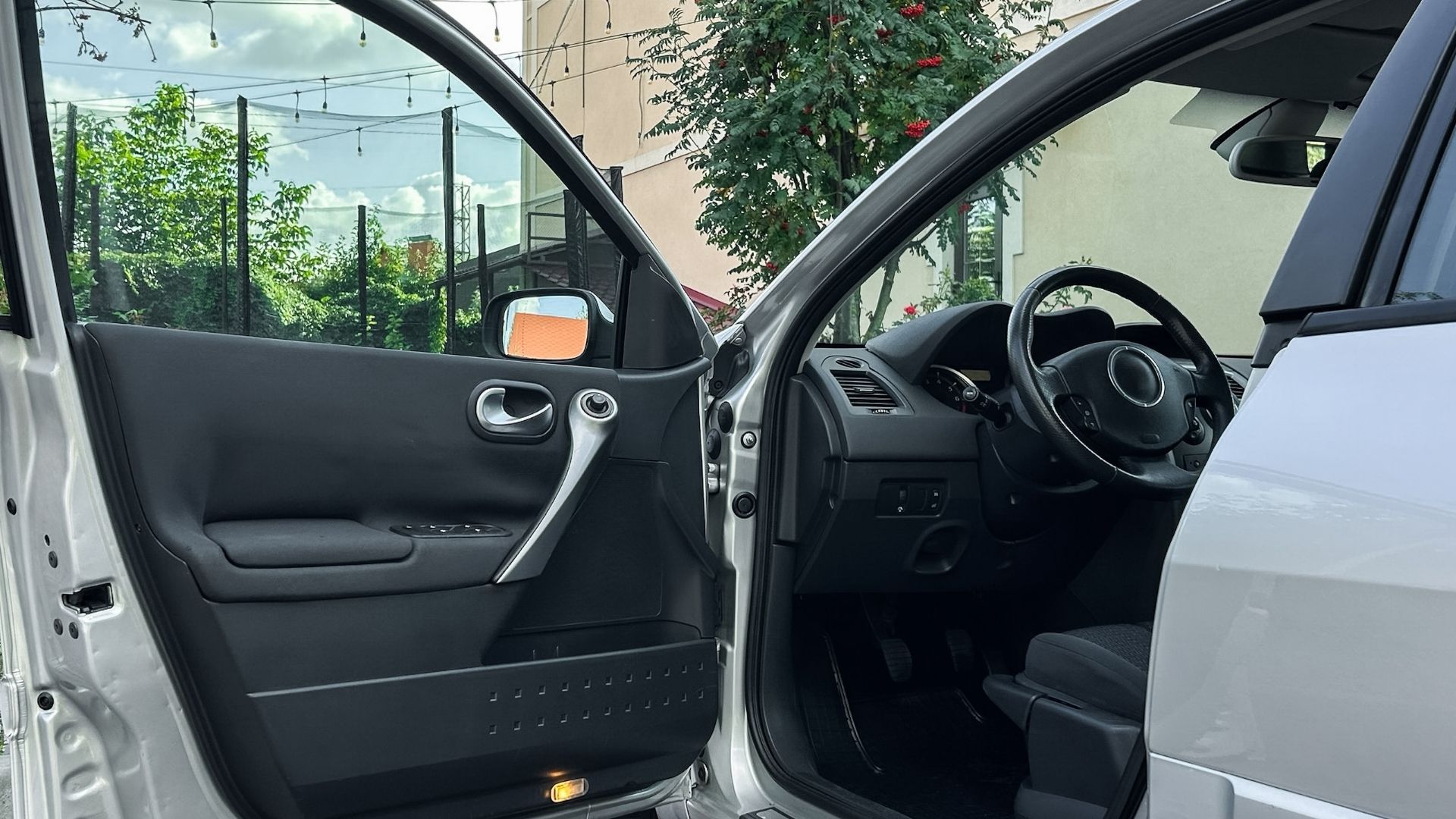 Open car door showing black interior and steering wheel, with a silver exterior parked outside.