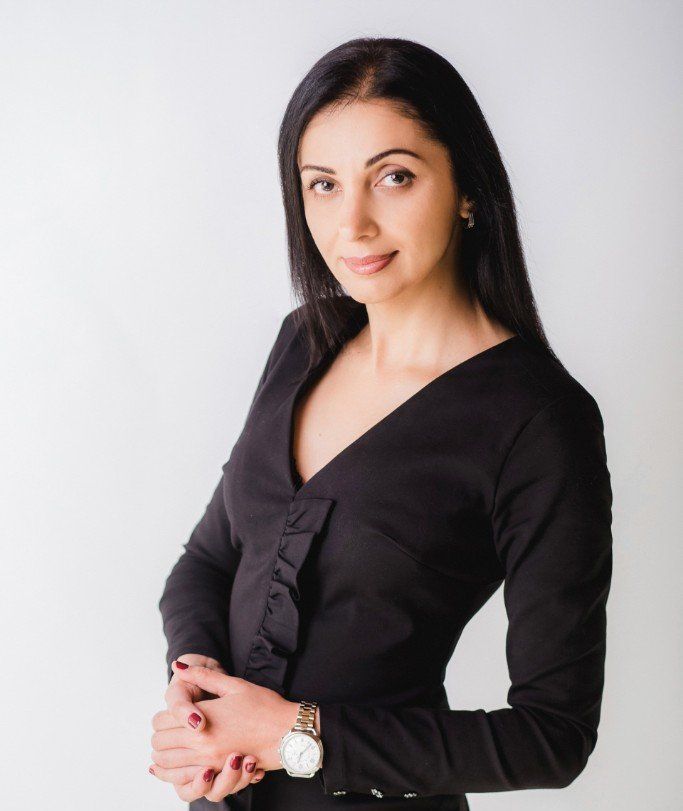 Eine Frau in einem schwarzen Kleid steht mit gefalteten Händen da.