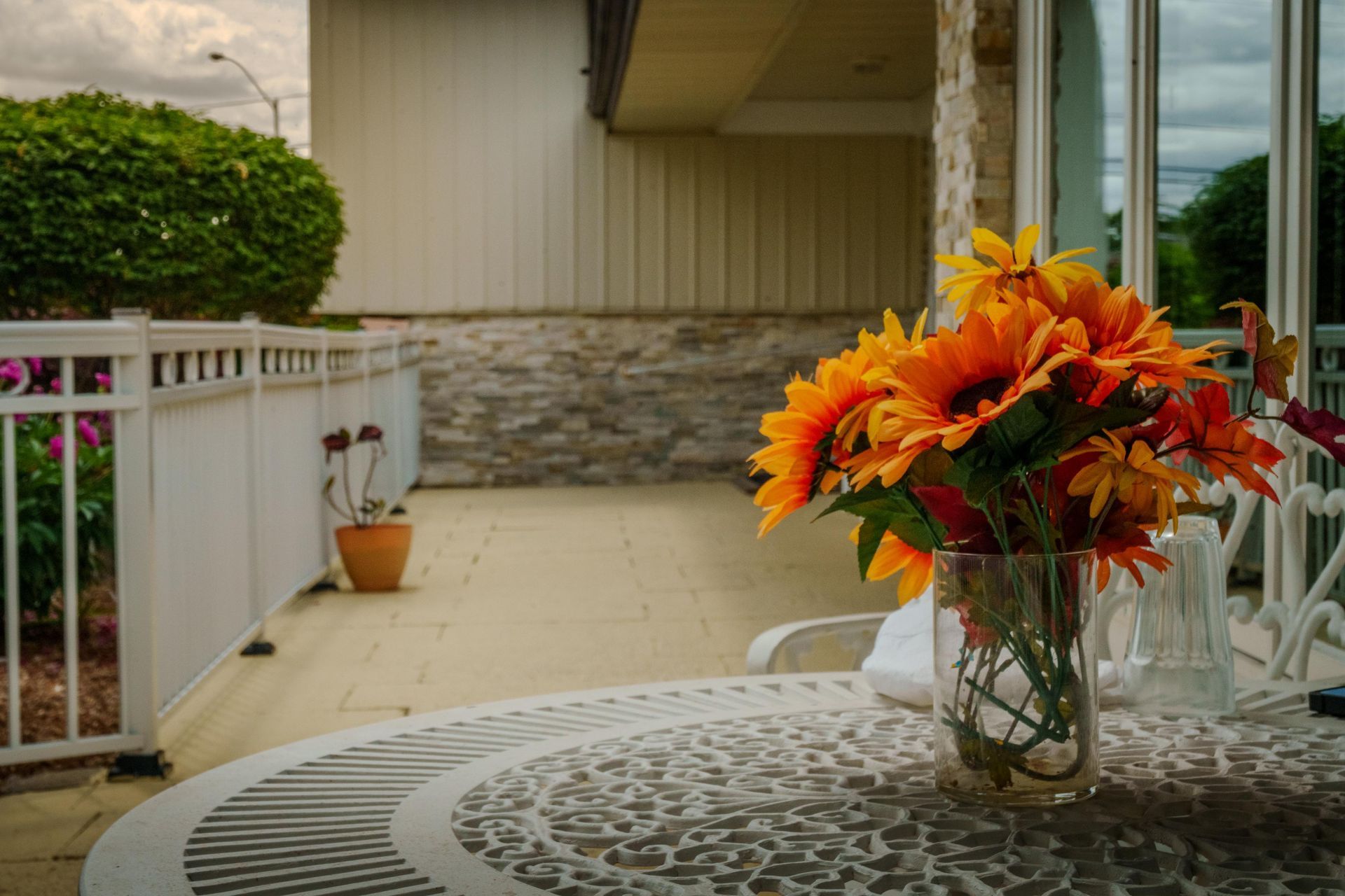 Patio table with orange flowers in a glass vase beside a white fence and stone wall