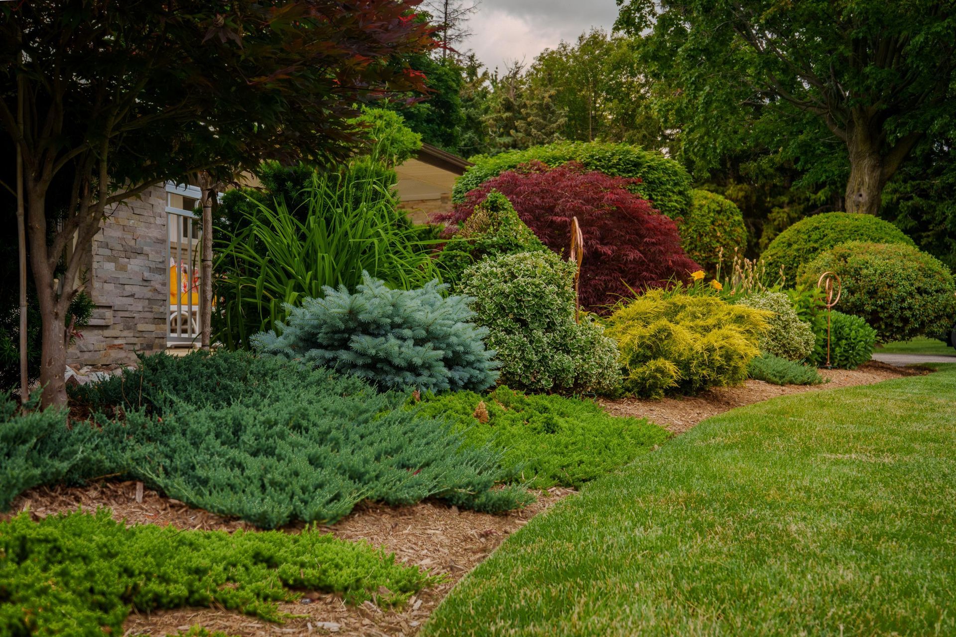 Lush landscaped garden with colorful shrubs, trees, and a green lawn beside a stone wall