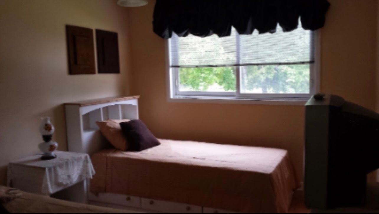 Bedroom with a bed, window, dark valance, and small side table in soft daylight
