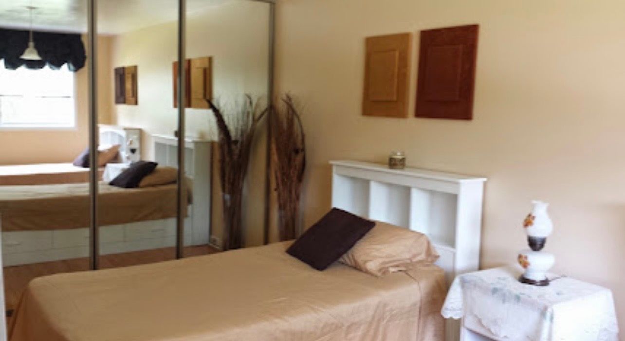 Bedroom with mirrored closet, twin bed, white mantel shelf, and side table with lamp and decor