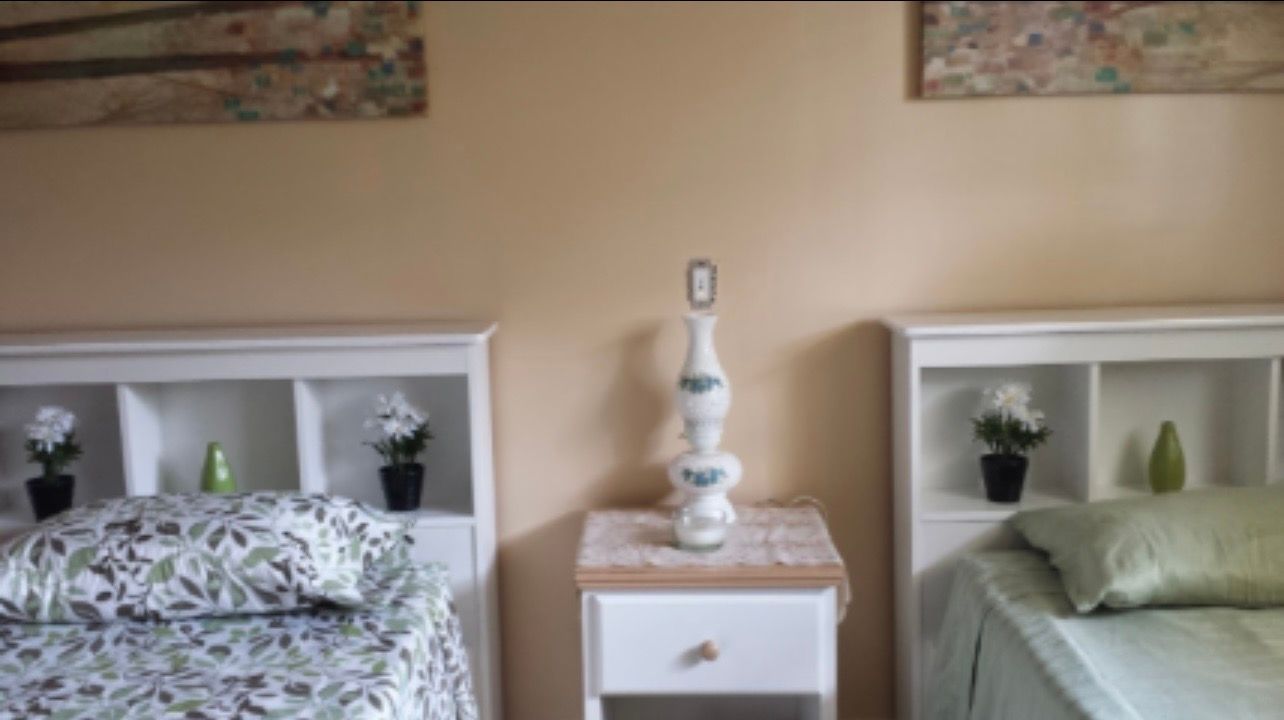 Two neatly made twin beds with white headboards and a small white nightstand between them.