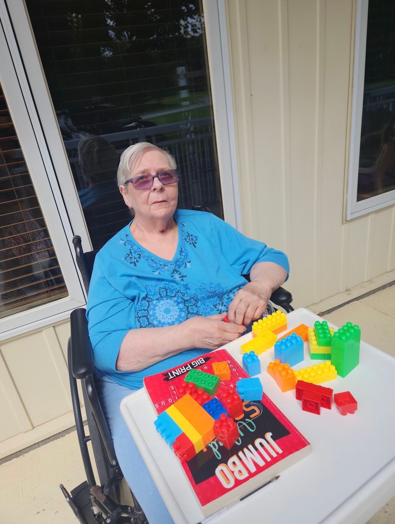 Woman at a table with colorful building blocks and a red-and-black book outdoors on a porch