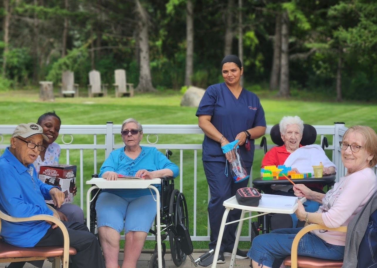 People seated outdoors around tables while a woman stands nearby, in a park-like setting.