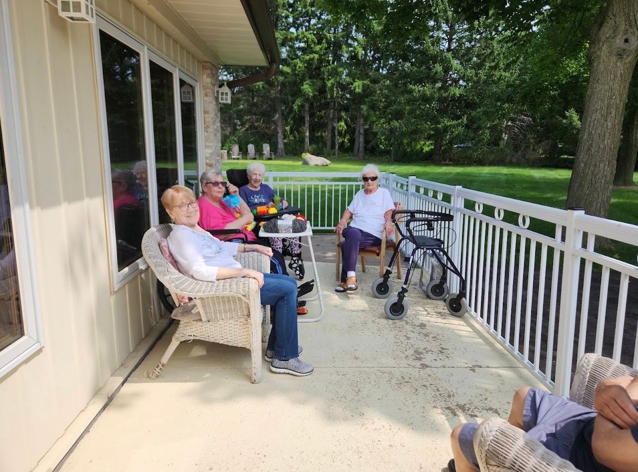People sitting on a porch with railings, trees and a yard in the background