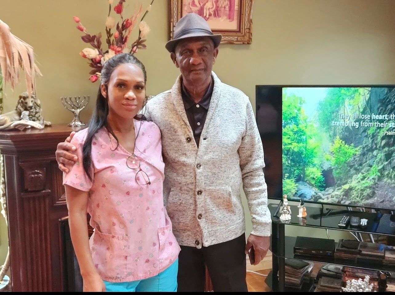 Two people standing together in a living room beside a TV displaying a green forest scene
