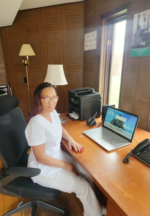 Person seated at a wooden desk in an office, using a laptop beside a phone and printer.