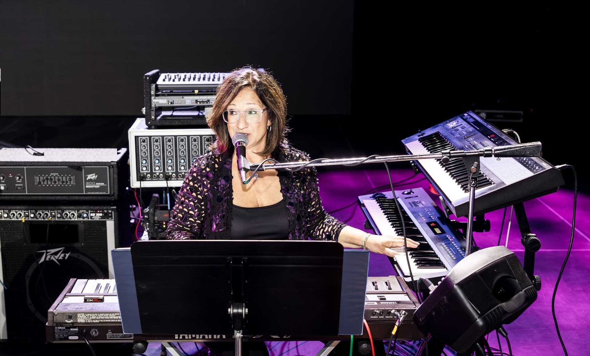 A woman is playing a keyboard and singing into a microphone on a stage.