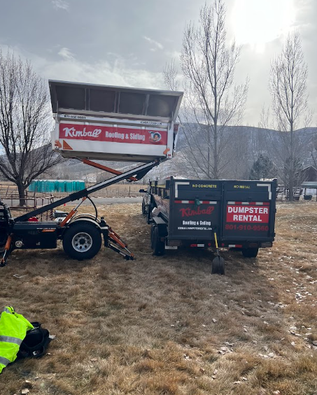 A truck with a dumpster lifting a full container in a field with a mountain backdrop. 