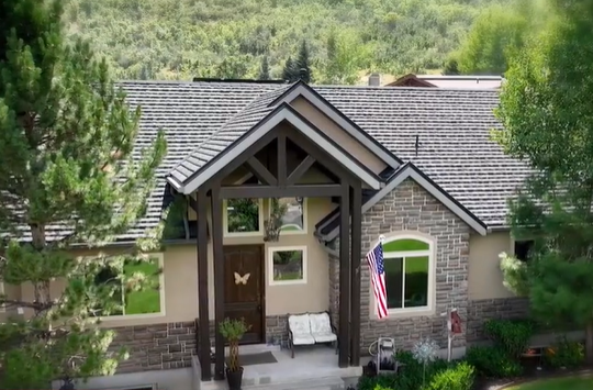 Building facade with windows and an American flag, set against a forested hillside.