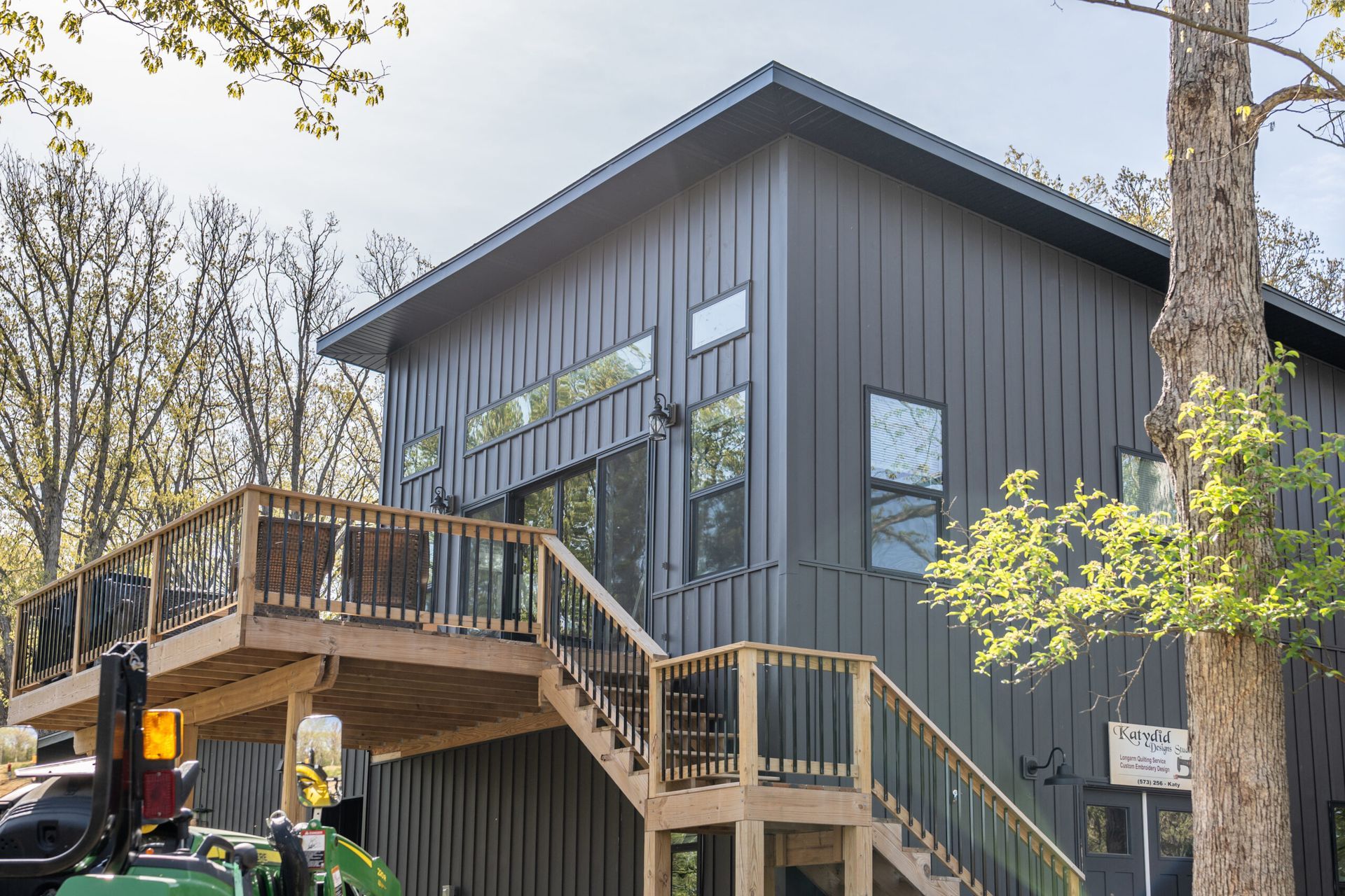 Modern two-story gray building with large windows and an elevated wooden deck and stairs among trees