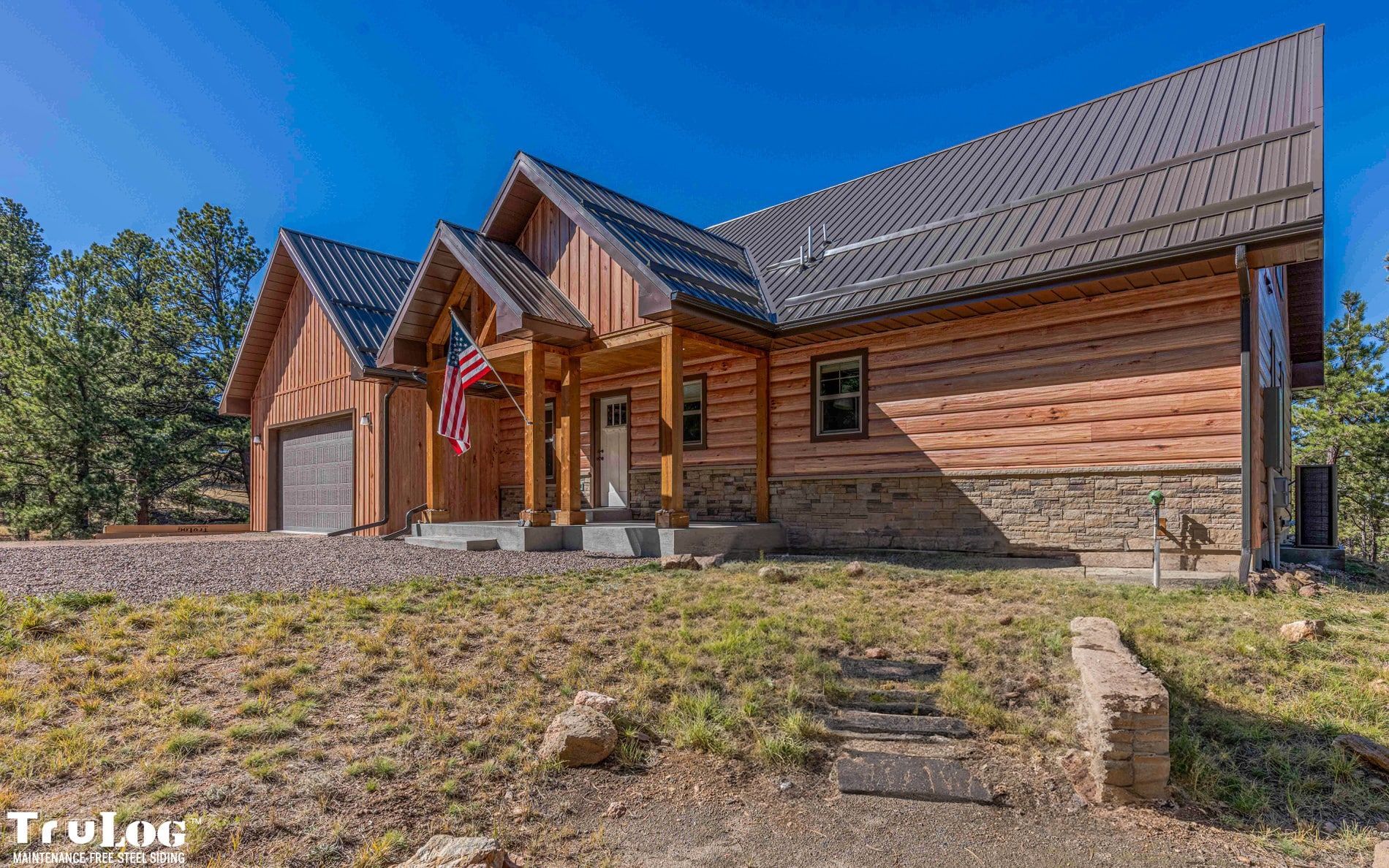 Log cabin-style house with brown siding, front porch, and American flag on a sunny day