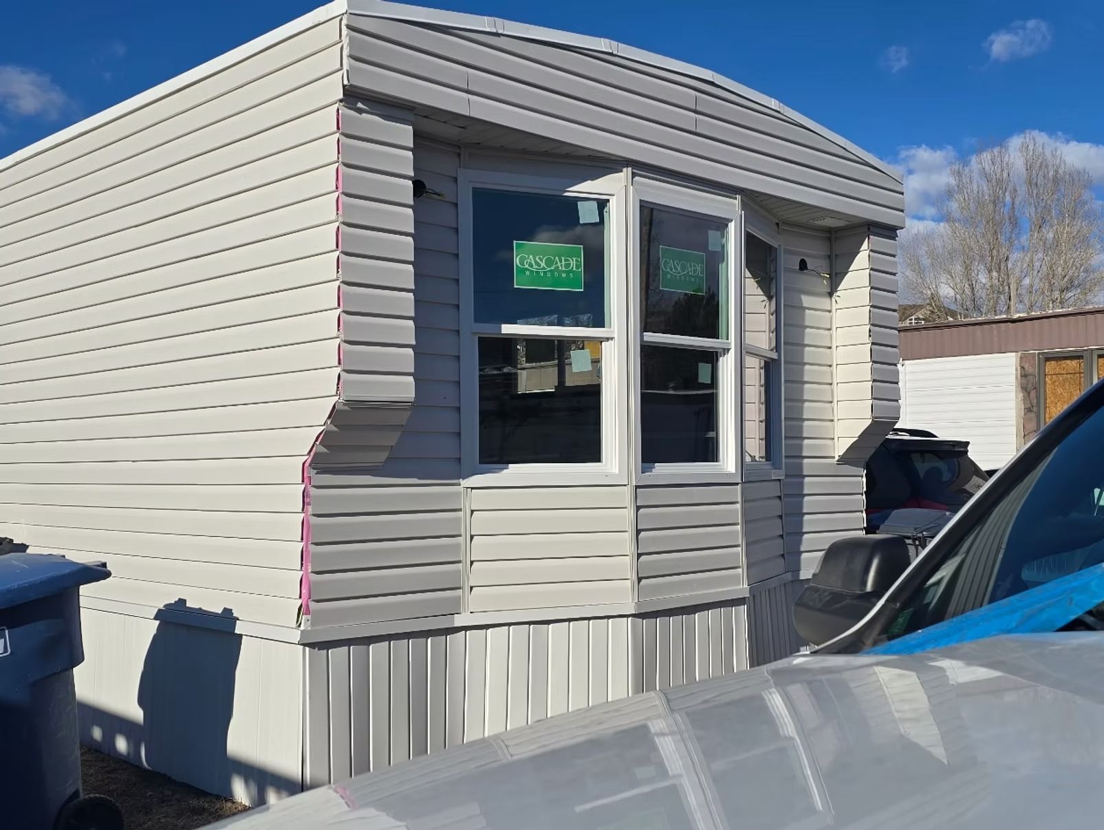 Mobile home with gray and white siding, bay window, and blue sky.