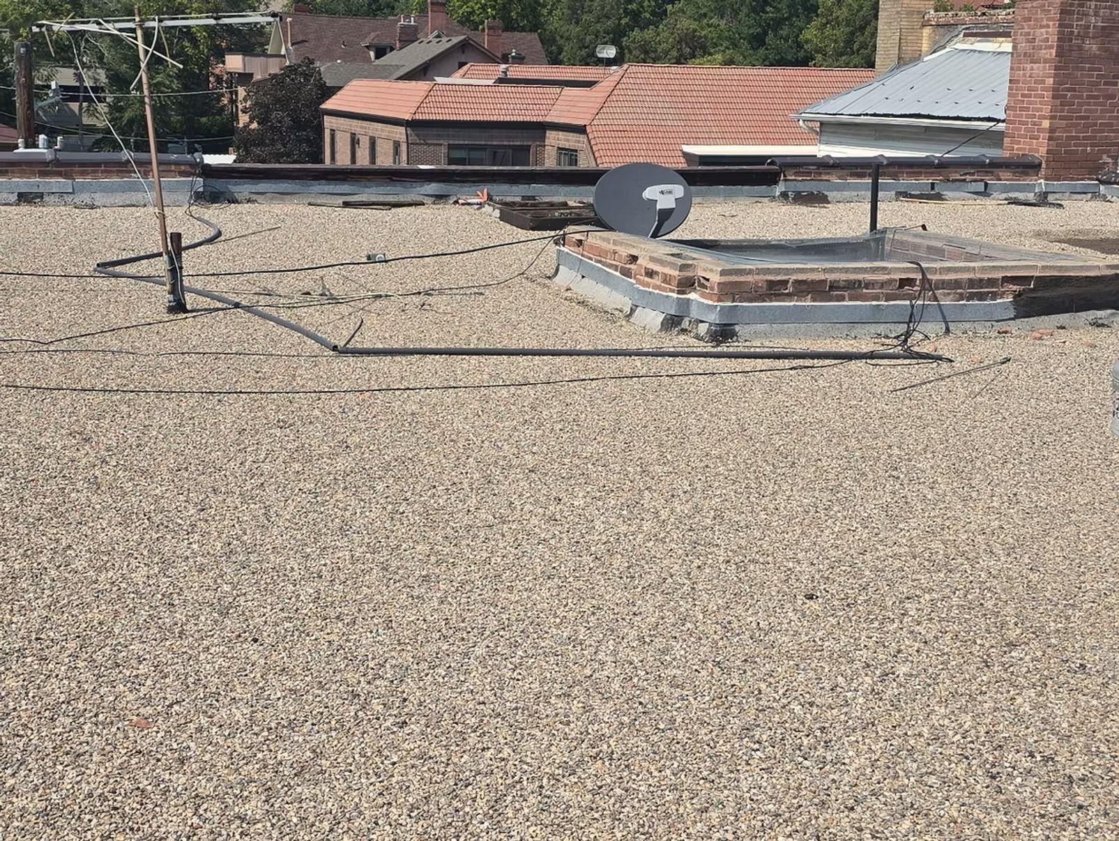 Gravel-covered flat roof with satellite dish, antenna, and brick chimney. Buildings in the background.